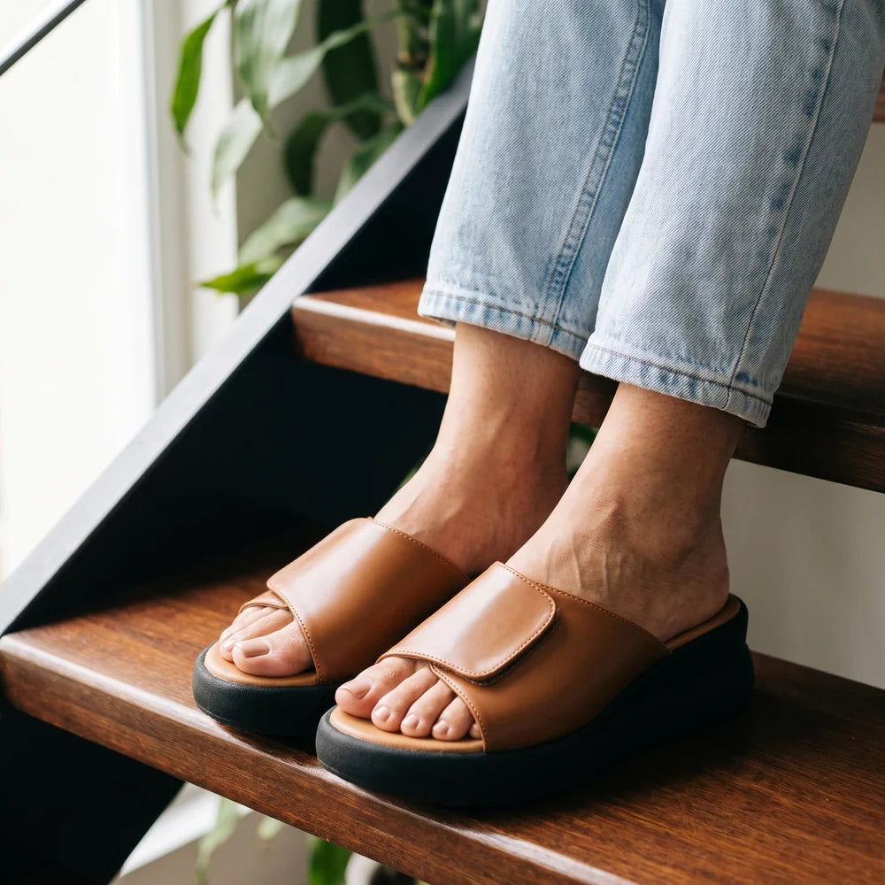 Mujer sentada en una escalera de madera con sandalias de plataforma color miel y jean claro